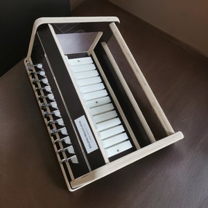 May include: A wooden music box with a white keyboard and a label that reads "SOLID LITTLE MASTER". The music box has a series of silver tuning pegs on the side.