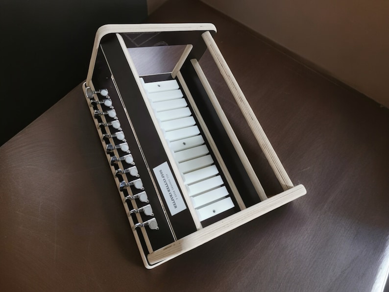 May include: A wooden music box with a white keyboard and a label that reads "SOLID LITTLE MASTER". The music box has a series of silver tuning pegs on the side.