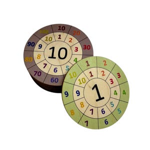 May include: Two wooden multiplication wheels. One is brown with numbers 1-10 and multiples of 10. The other is green with numbers 1-10. The center of each wheel has a large number, 10 and 1 respectively.
