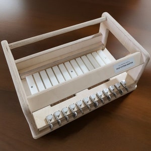 May include: A wooden soap cutter crafter with a white cutting surface and a rack for storing cutters. The crafter has a label that reads "All Natural Soaps & SOAP CUTTER CRAFTERS".