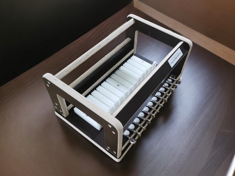May include: A wooden storage rack with a black base and white dividers. The rack is designed to hold guitar tuning pegs. The rack has a label that reads "Guitar Tuning Pegs".