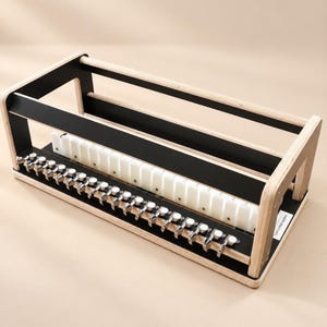 Può includere: Un telaio rettangolare in legno con una cornice in legno chiaro naturale e pannelli interni neri. Presenta una fila di perni di tensione in metallo argentato lungo il bordo anteriore e una barra separatrice in plastica bianca all'interno.