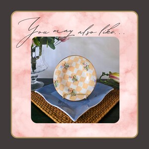 May include: A decorative plate with a yellow and white checkered pattern and floral accents, displayed on a gold stand. The plate sits atop a blue square plate, with a woven mat underneath. The image has the text "You may also like..."