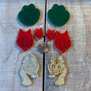 Peut inclure: Un ensemble de six breloques en acrylique représentant des animaux, dont deux empreintes de pattes vertes, deux têtes de loup rouges et deux têtes de tigre dorées.