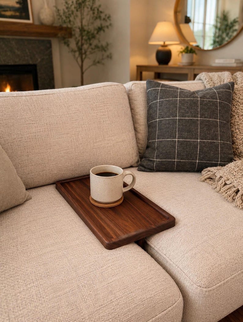 May include: A rectangular dark brown wooden tray rests on a beige fabric sofa. A speckled off-white ceramic mug filled with black coffee sits on a small round wooden coaster placed on the center of the tray.