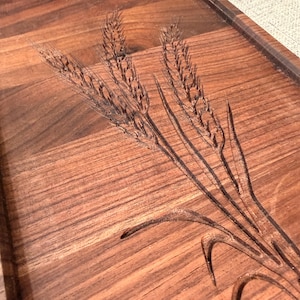 May include: A rectangular dark brown wooden serving tray featuring a detailed laser-engraved design of three stalks of wheat. The tray has a smooth finish with visible wood grain patterns and a raised border edge along the perimeter.