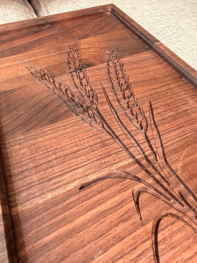 May include: A rectangular dark brown wooden serving tray featuring a detailed laser-engraved design of three stalks of wheat. The tray has a smooth finish with visible wood grain patterns and a raised border edge along the perimeter.