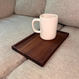 May include: A rectangular dark brown wooden tray with a smooth finish and a raised border edge, featuring a single white ceramic mug with a rounded handle placed on top of the tray surface. The tray is designed to rest flat on a surface.