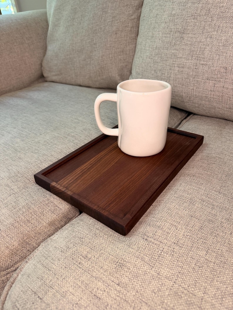 May include: A rectangular dark brown wooden tray with a smooth finish and a raised border edge, featuring a single white ceramic mug with a rounded handle placed on top of the tray surface. The tray is designed to rest flat on a surface.