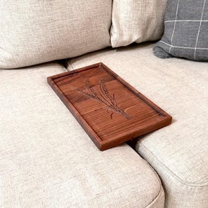 May include: A rectangular wooden tray with a carved wheat design. The tray is made of dark brown wood and has a raised edge. The wheat design is centered on the tray.