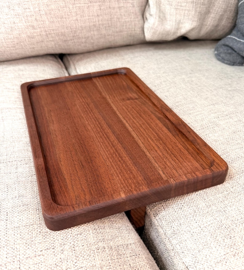 May include: A rectangular wooden tray with a smooth, dark brown finish and a raised border edge. The tray features a flat, recessed surface with visible wood grain patterns and a sturdy, solid construction designed for placement on flat surfaces.