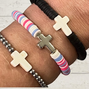 May include: Three bracelets with cross charms. One bracelet is black, one is silver, and one is white, pink, and blue.