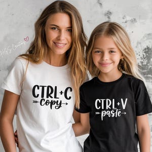 May include: Two people wearing matching shirts. The person on the left is wearing a white shirt with the text "CTRL+C copy" printed on it. The person on the right is wearing a black shirt with the text "CTRL+V paste" printed on it.