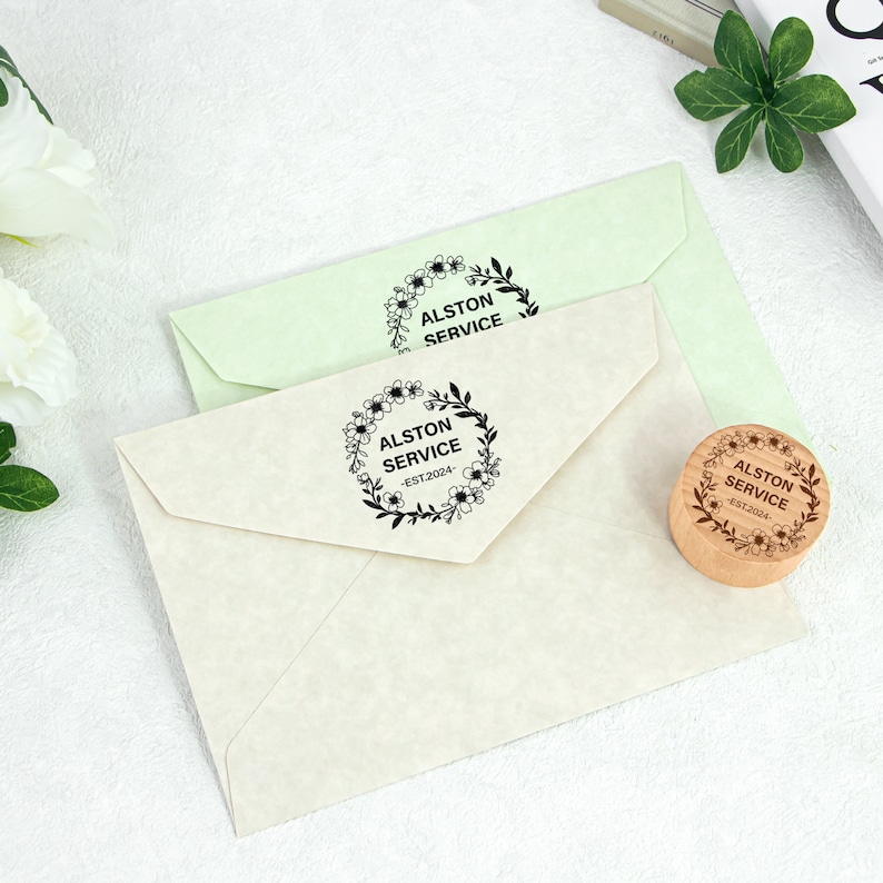 May include: A close-up of two envelopes with a floral wreath stamp that says "Alston Service - Est 2024".
