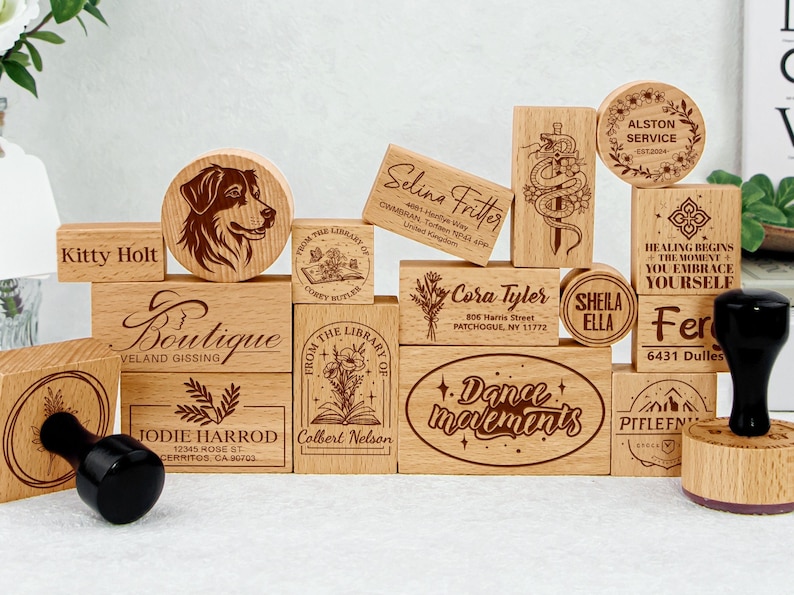 May include: A collection of wooden stamps with various designs and text, including names, addresses, and phrases like "Boutique", "Dance Movements", and "From the Library of". The stamps are arranged in a random pattern on a wooden surface.