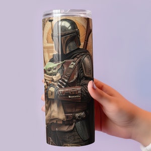 Puede incluir: Un vaso de acero inoxidable con una imagen colorida de un personaje mandaloriano sosteniendo una peque&ntilde;a criatura verde. La imagen est&aacute; impresa en todo el vaso.