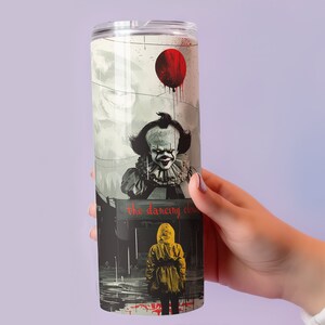 May include: A stainless steel tumbler with a graphic of Pennywise the Dancing Clown from the movie "IT". The graphic shows Pennywise holding a red balloon and a child in a yellow raincoat looking up at him. The text "the dancing clown" is printed on the tumbler.