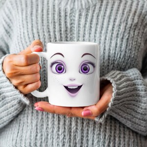 以下が含まれることがあります： 白いセラミック製のマグカップに、漫画の顔がプリントされています。顔は紫色の目、ピンクの唇、そばかすがあります。