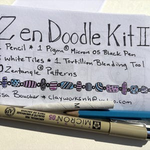 May include: A Zen Doodle Kit II set featuring a white card with black text listing contents: 1 Pencil, 1 Pigma Micron 05 Black Pen, 5 white tiles, 1 Tortillion Blending Tool, and 10 Zentangle Patterns. Includes a Pigma Micron 05 pen and a pencil.