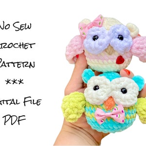 Op de afbeelding: Twee handgemaakte gehaakte uilenspeeltjes. De bovenste uil is crème, roze en wit met een roze strik. De onderste uil is turquoise, groen en wit met een roze strik. Tekst links zegt "No Sew Crochet Pattern Digital File PDF".