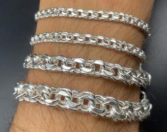 Puede incluir: Se muestran cuatro pulseras de cadena de plata de diferentes diseños. Las pulseras, hechas de metal pulido, se llevan en una muñeca. Las cadenas presentan varios estilos de eslabones, incluyendo formas redondas y ovaladas.