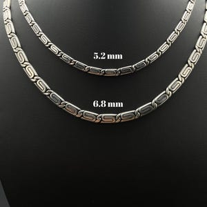 Puede incluir: Dos collares plateados con un dise&ntilde;o repetitivo de &oacute;valos y barras, presentados sobre un fondo negro. Los collares miden 5,2 mm y 6,8 mm de ancho. La joyer&iacute;a se presenta sobre un busto de maniqu&iacute;.