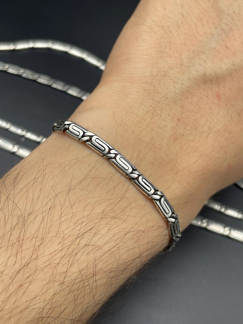 Puede incluir: Una pulsera de plata con un intrincado patr&oacute;n repetitivo de formas de 'S' estilizadas. La pulsera se lleva en una mu&ntilde;eca, mostrando su dise&ntilde;o y artesan&iacute;a. Joyer&iacute;a de plata.