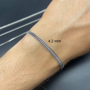 May include: A silver-colored bracelet with a 4.2 mm width is displayed on a wrist. The bracelet has a woven chain design. The background is a dark gray color.
