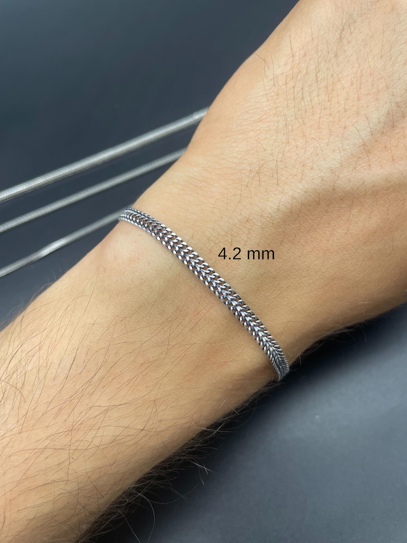 May include: A silver-colored bracelet with a 4.2 mm width is displayed on a wrist. The bracelet has a woven chain design. The background is a dark gray color.