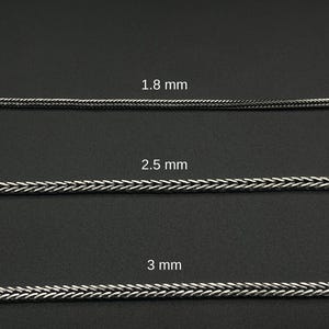May include: Three silver-colored chain samples with varying thicknesses: 1.8 mm, 2.5 mm, and 3 mm. The chains have a woven or braided design, displayed against a dark background. The image showcases the different chain sizes.