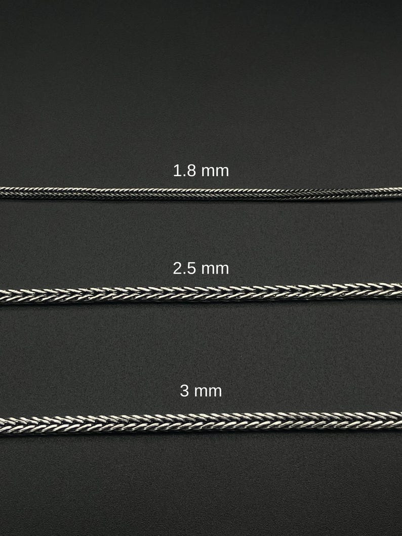May include: Three silver-colored chain samples with varying thicknesses: 1.8 mm, 2.5 mm, and 3 mm. The chains have a woven or braided design, displayed against a dark background. The image showcases the different chain sizes.