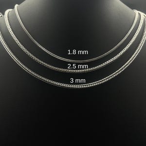 May include: Three silver-colored chain necklaces of varying thicknesses are displayed on a black mannequin. The chains are 1.8 mm, 2.5 mm, and 3 mm thick. The chains have a woven design.