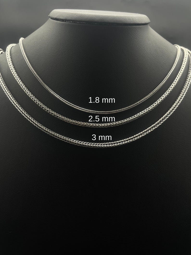 May include: Three silver-colored chain necklaces of varying thicknesses are displayed on a black mannequin. The chains are 1.8 mm, 2.5 mm, and 3 mm thick. The chains have a woven design.