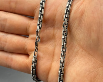May include: A silver chain necklace with a box chain design. The chain is made of small, square links that are connected together.