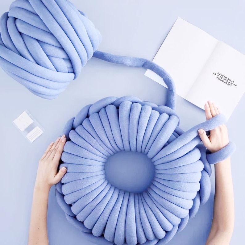 May include: A light blue yarn donut cushion with a large hole in the center. The cushion is made from a thick, chunky yarn and is perfect for adding a touch of texture and color to any room.