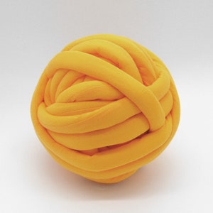 May include: A large, bright yellow ball of yarn made from thick, soft fabric. The yarn is tightly wound into a ball shape.