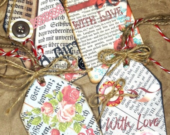 May include: A collection of handmade gift tags with a vintage aesthetic. The tags feature floral designs, text from old books, and decorative buttons. Each tag is tied with twine and red and white string.