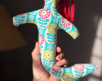 May include: A handmade mermaid doll with a patterned fabric body in shades of blue, pink, and yellow. The doll has red hair and a whimsical design. The doll is held in a person's hand.