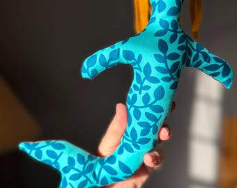 May include: A handmade mermaid doll with a teal body and a dark blue leaf pattern. The doll has a yellow head and tail. The doll is made of fabric and is soft to the touch. The mermaid doll is a unique and whimsical toy.