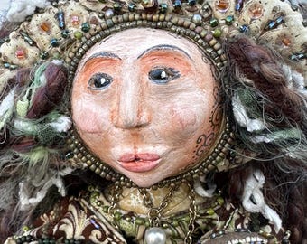 May include: A handmade doll with a beaded crown, a brown and green patterned dress, and a pearl necklace. The doll has a painted face with brown eyes and a pink mouth.