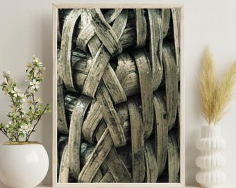 May include: A framed close-up of woven material in shades of gray and beige. The texture is intricate, with overlapping strips creating a basket-like pattern. The artwork is displayed on a light-colored shelf, with a white vase and decorative plants.