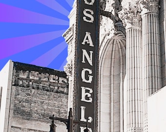 May include: A vertical sign reading "LOS ANGELES" in white letters against a dark background. The sign is mounted on a building with ornate architectural details, including columns and arches. A street lamp is in the foreground, and a blue and purple burst pattern is in the background.