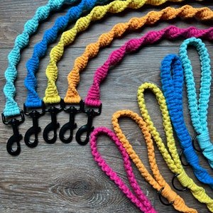 Może przedstawiać: Sześć kolorowych, szydełkowych smyczy dla psa z czarnymi metalowymi klamrami. Smycze są ułożone w tęczę, z kolorami: turkusowym, niebieskim, żółtym, pomarańczowym, różowym i czerwonym.