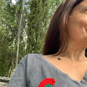May include: A gray t-shirt with a red and green crocheted flower pinned to the front.