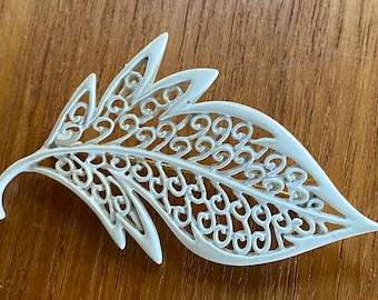 May include: White filigree leaf brooch with a delicate, intricate design. The brooch is made of metal and has a gold-tone finish.