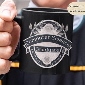 Può includere: Tazza in ceramica nera con manico, con un design per un laureato in Informatica. Il design include un cappello di laurea, foglie di alloro e il testo "Computer Science Graduate Kayleigh C Class of 2026".