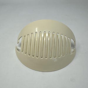 May include: A cream-colored hair comb with a half-circle shape. The comb features evenly spaced teeth and curved edges. The design includes two small hooks on either side of the comb.