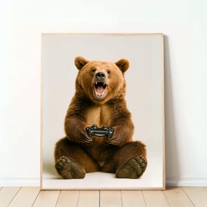 Könnte beinhalten: Gerahmter Druck, der einen braunen Bären zeigt, der sitzt und einen schwarzen Videospiel-Controller hält. Der Bär hat das Maul offen, als würde er brüllen. Der Druck hat einen hellen Holzrahmen.