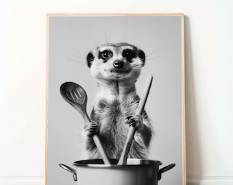 May include: Black and white framed print of a meerkat holding wooden spoons over a pot. The meerkat is centered in the frame, with the pot at the bottom. The background is a solid light gray.