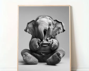 May include: Black and white framed print featuring a baby elephant sitting cross-legged and playing a video game. The elephant is holding a game controller with its trunk and appears focused. The print has a light wood frame and a neutral background.
